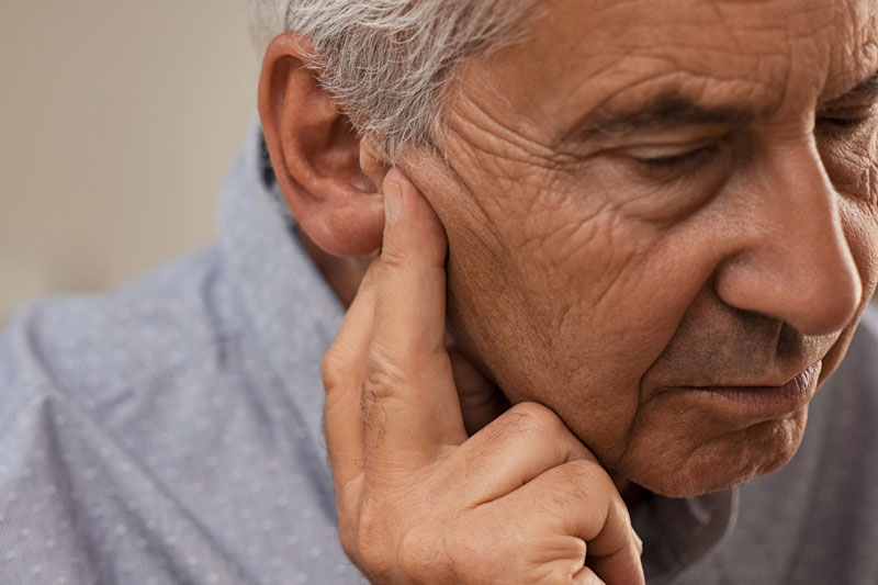 A man holds his ear from a painful medical condition.