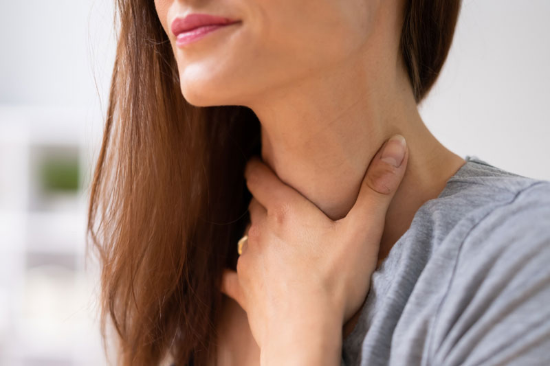 A woman suffering from a speech-related health condition touches her painful throat area.