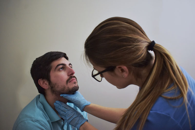 A speech medicine specialist examines a man’s throat and neck in a medical office.