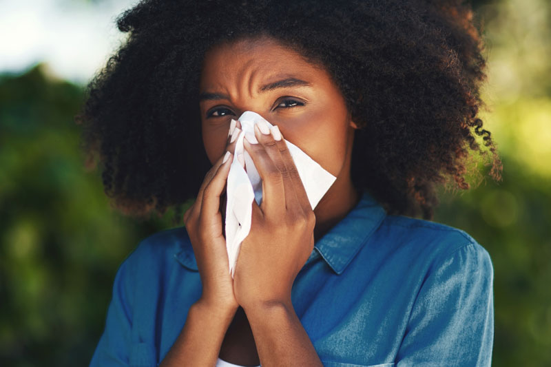 A woman suffering from allergies blows her nose.