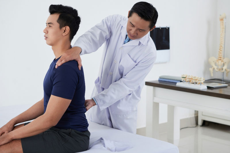 A doctor treats a patient for spine pain in a medical exam room.
