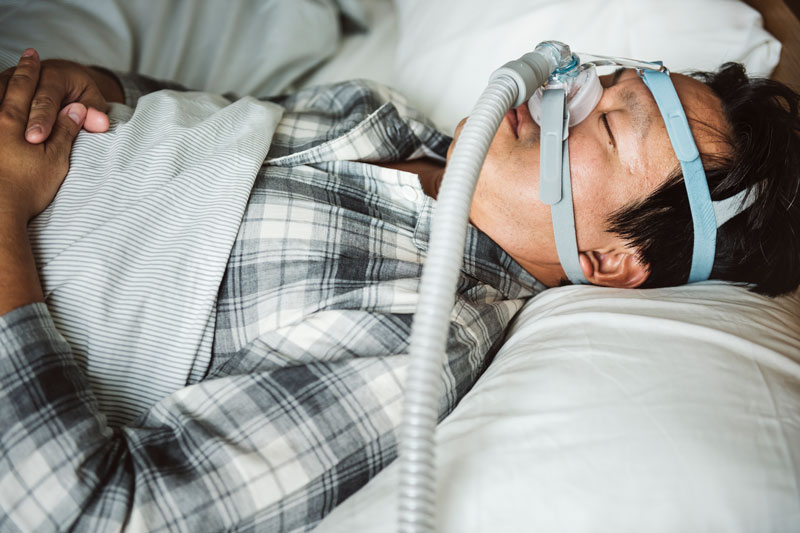 A man with sleep apnea rests comfortably wearing a CPAP machine to aid with snoring.