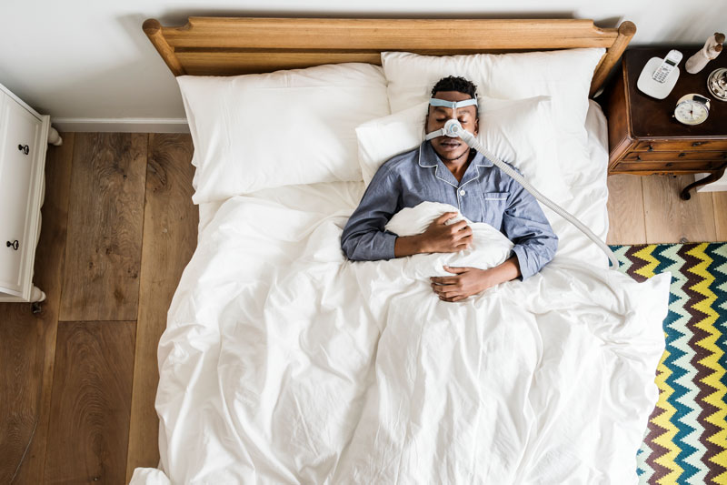 A man with sleep apnea sleeps in his bed with a medical device to prevent snoring.