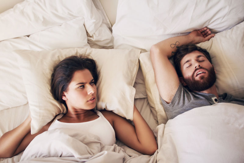A woman is annoyed at her partner for snoring loudly in their bed.